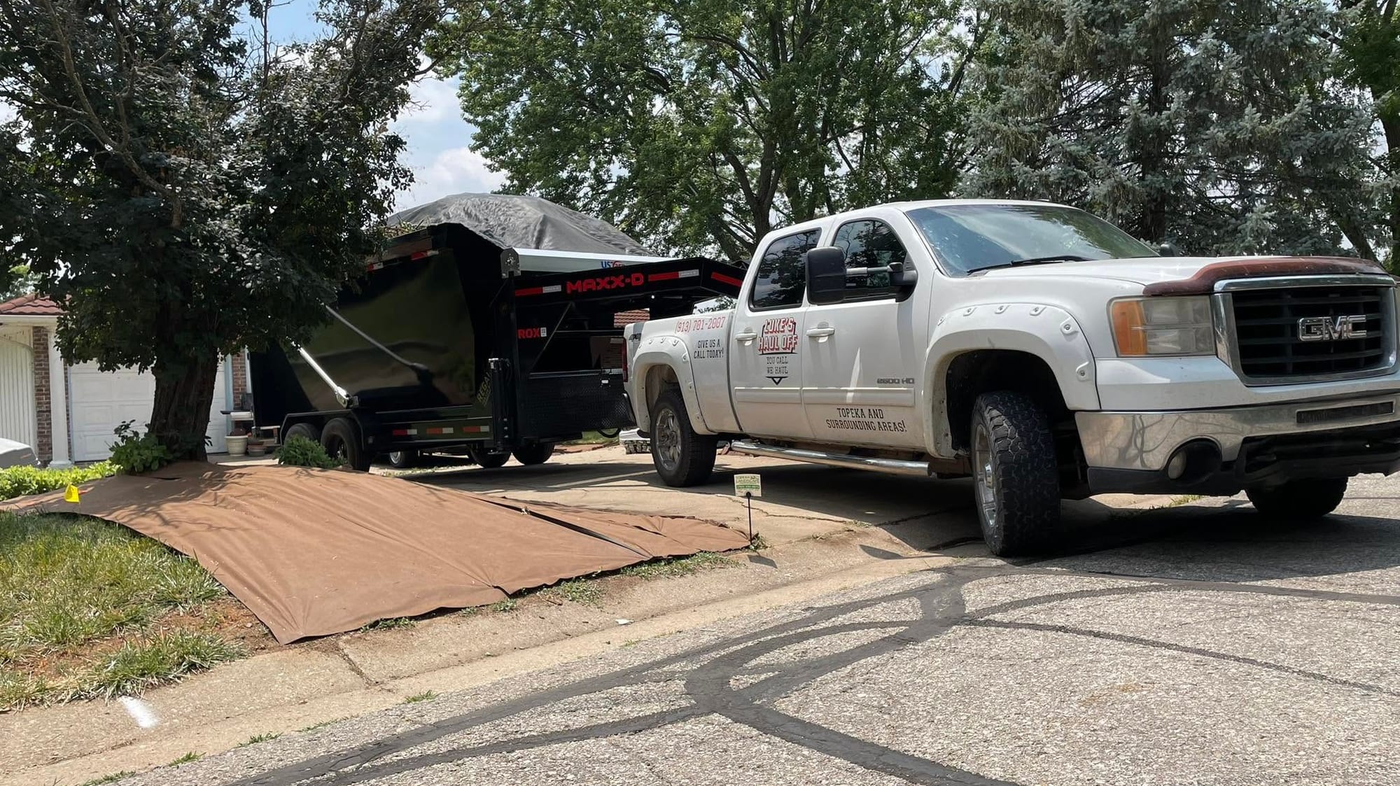 Setting a roll-off dumpster on a driveway, with a tarp down to protect the lawn