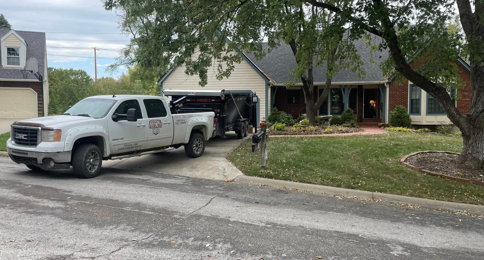 Luke's Haul Off truck backing a roll-off dumpster into a home driveway